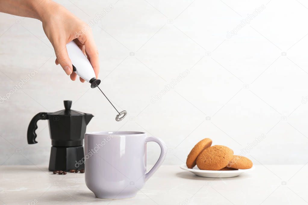 Woman using milk frother in cup on table. Space for text
