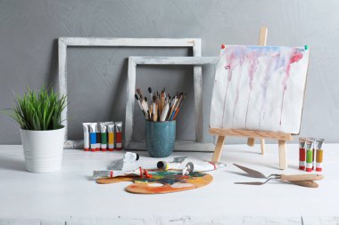 Şövale soyut resim ve profesyonel sanat malzemeleri gri arka plan karşı masada dizi