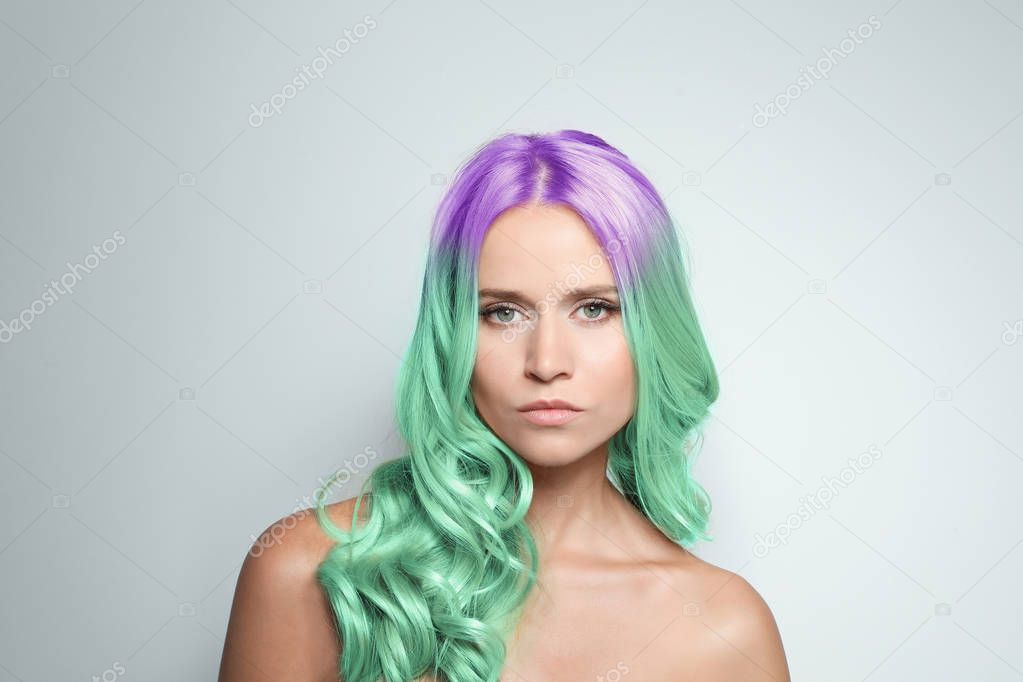 Portrait of young woman with dyed long curly hair on grey background. Trendy hairstyle design 