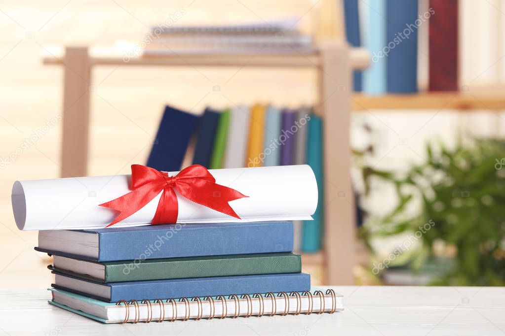 Graduate diploma with books and notebook on table against blurred background