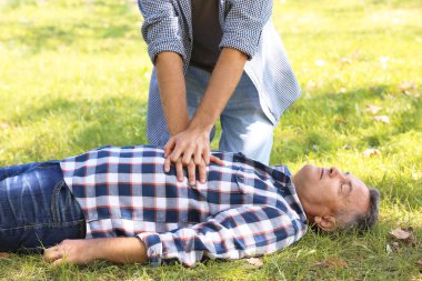 Yoldan geçen biri dışarıda baygın bir adama kalp masajı yapıyor. İlk yardım