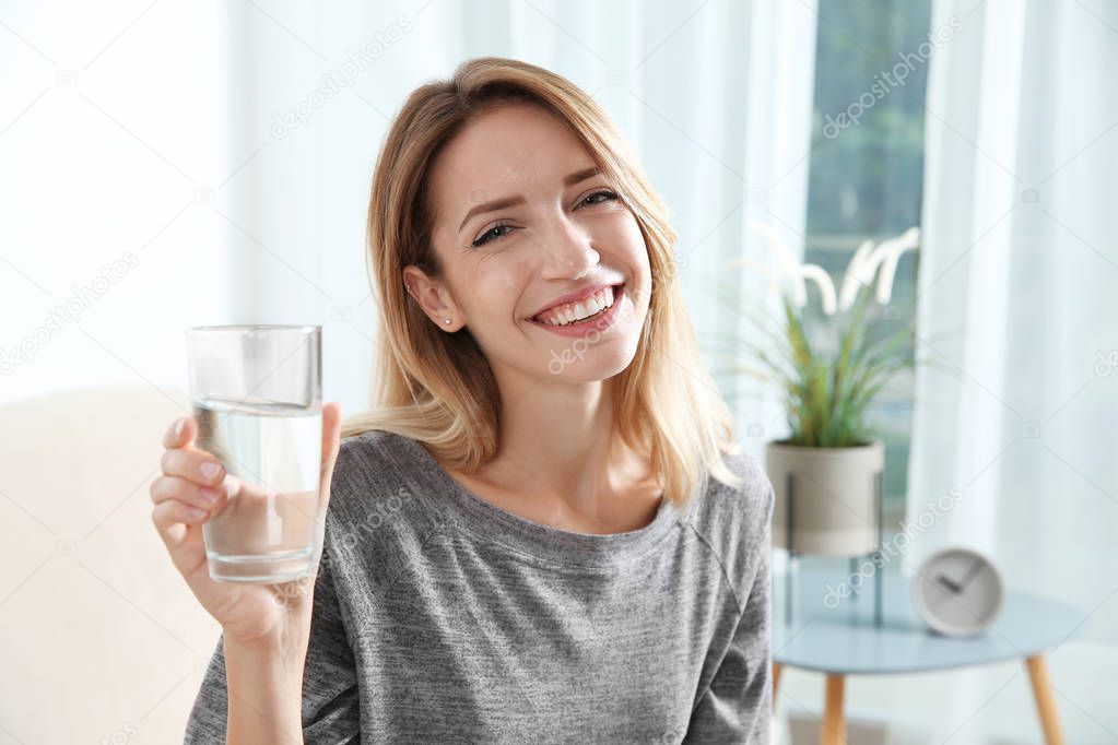 Young woman holding glass with clean water at home
