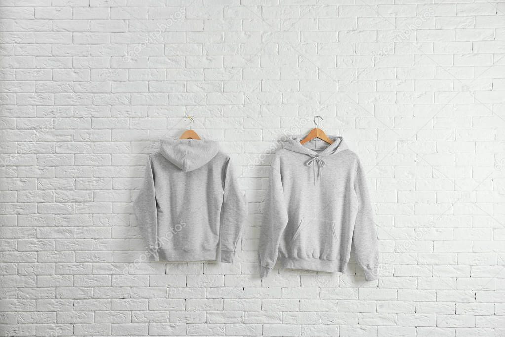New hoodie sweaters with hangers on brick wall. Mockup for design