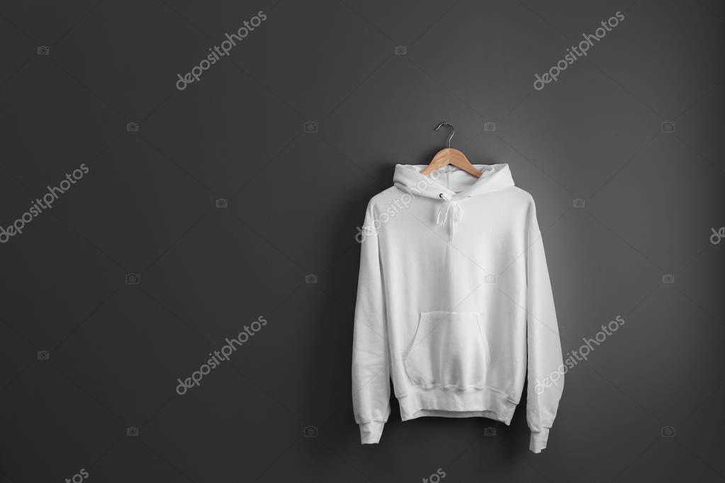 New hoodie sweater with hanger on grey wall. Mockup for design