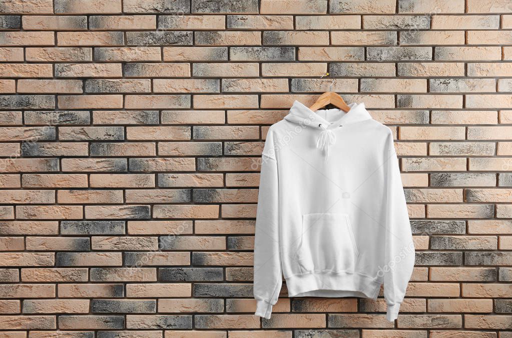 New hoodie sweater with hanger on brick wall. Mockup for design
