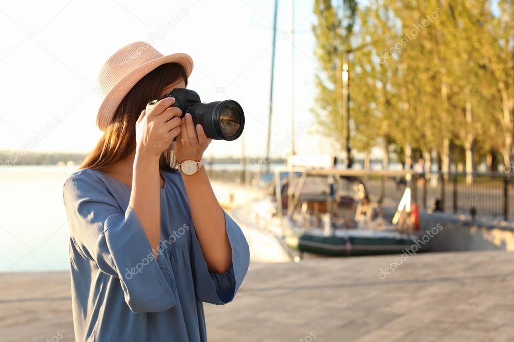 Young female photographer taking photo with professional camera at pier. Space for text