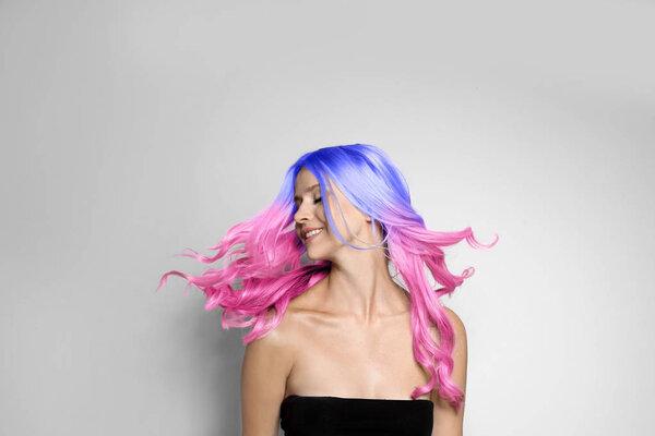 Portrait of smiling young woman with dyed long curly hair on grey background. Trendy hairstyle design 