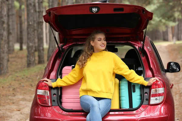 Araba bagajında oturan güzel genç kadın bavul orman yolu üzerinde yüklü