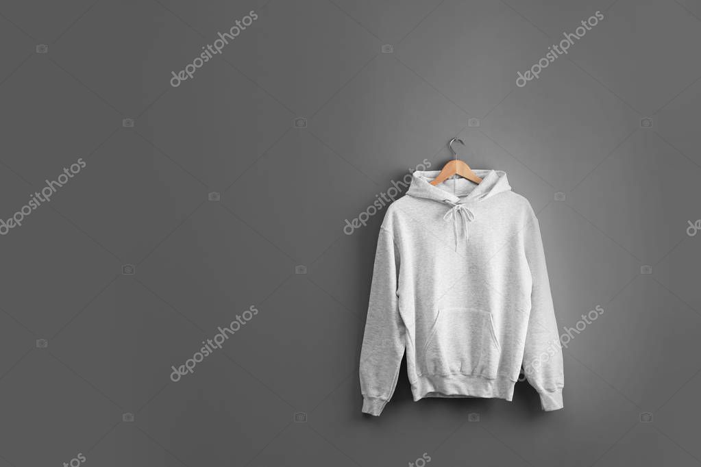 New hoodie sweater with hanger on grey wall. Mockup for design