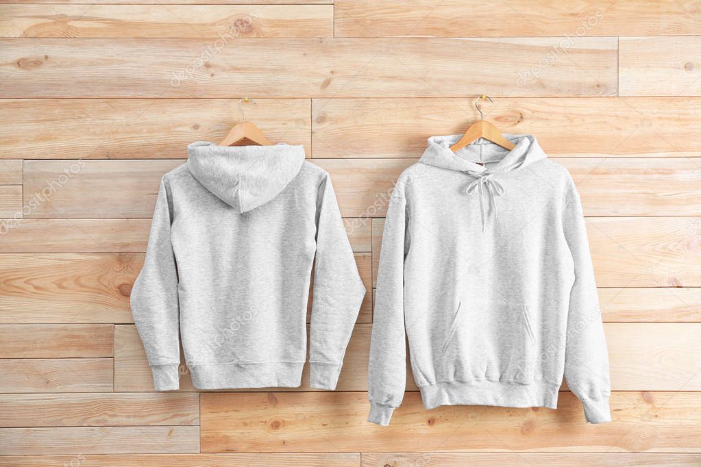 New hoodie sweaters with hangers on wooden wall. Mockup for design