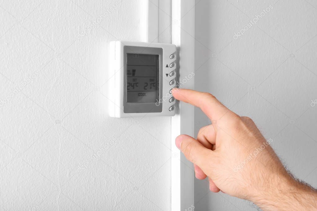 Man adjusting thermostat on white wall, closeup. Heating system