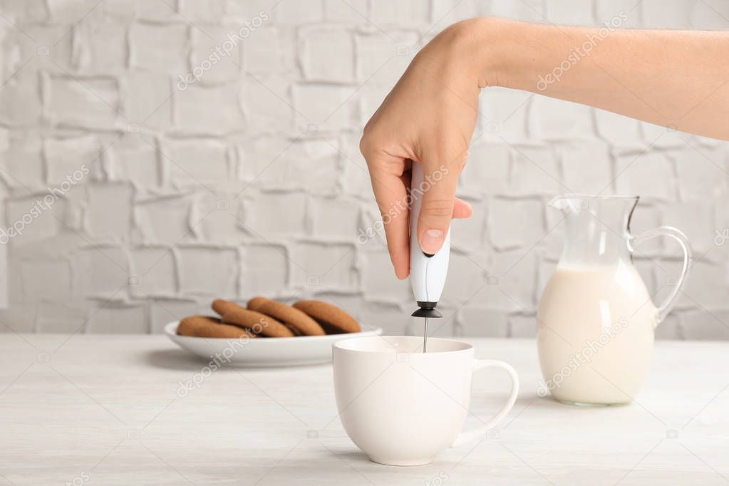 Woman using milk frother device in cup on table
