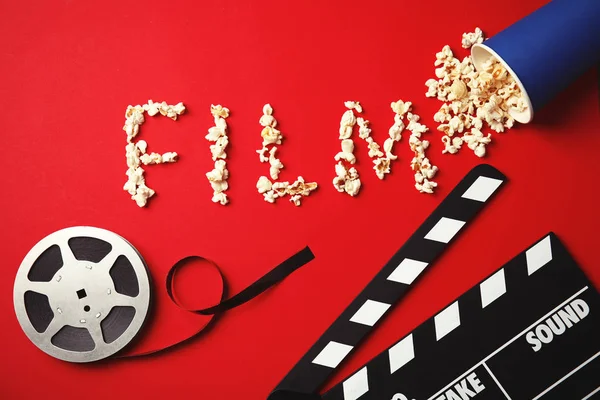 Flat lay composition with word FILM made of popcorn, reel and clapperboard on color background. Cinema snack