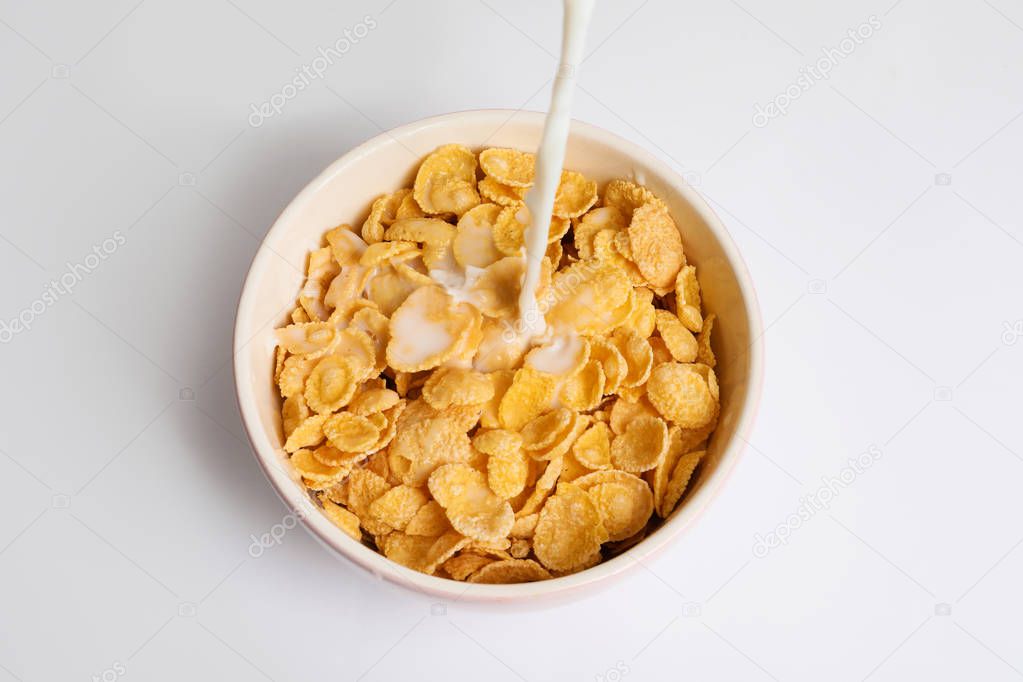 Milk pouring into bowl with crispy cornflakes on white background