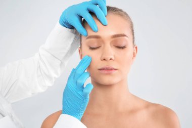 Doktor Genç kadın yüzü beyaz arka plan üzerinde kozmetik cerrahi daha önce incelenmesi