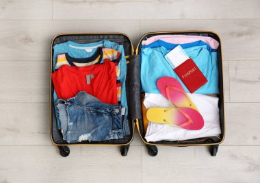 Çanta yazlık giysiler ve pasaport ile ahşap arka planda, üstten görünüm Paketli