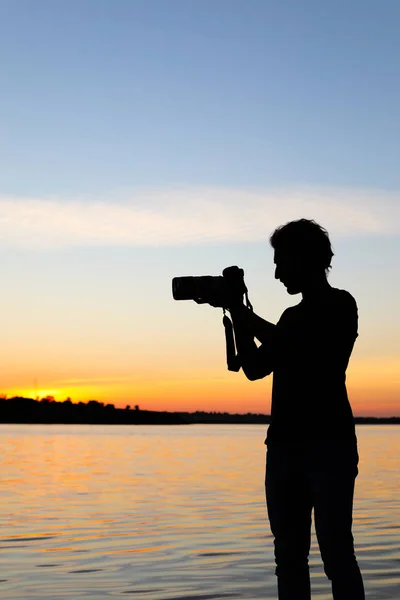 Young male photographer taking photo of riverside sunset with professional camera outdoors