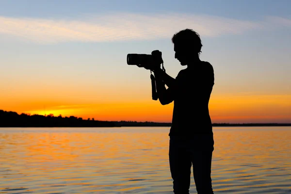 Young male photographer taking photo of riverside sunset with professional camera outdoors