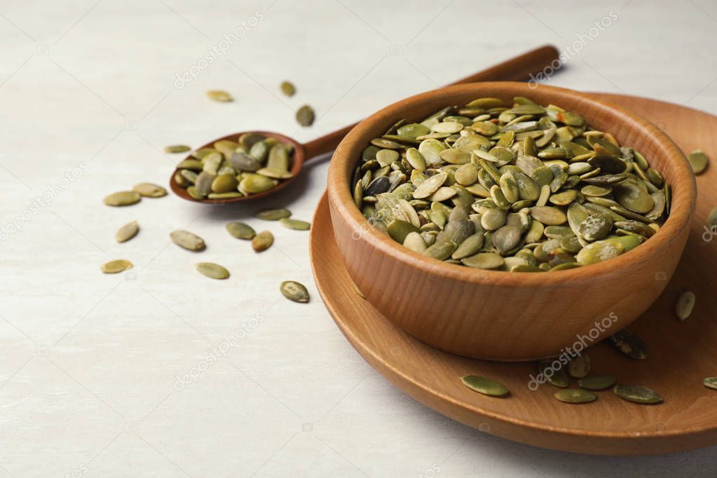 Shelled raw pumpkin seeds in dish on light background