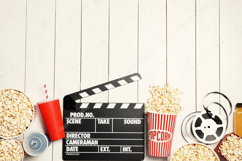 Flat lay composition with popcorn, cinema clapperboard and space for text on white wooden background