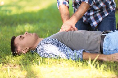 Yoldan geçen biri dışarıda baygın bir adama kalp masajı yapıyor. İlk yardım