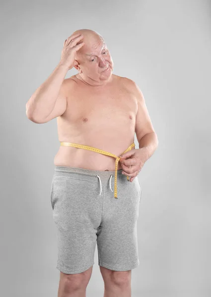 在灰色背景的测量带的脂肪高级男子 — 图库照片