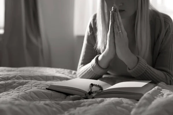 Religious young woman praying over Bible in bedroom. Black and white effect