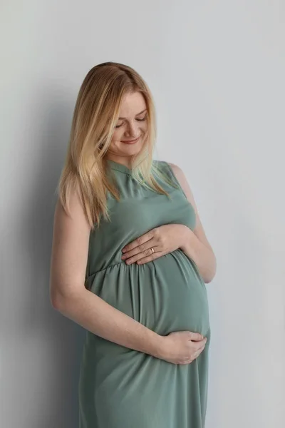年轻怀孕妇女抚摸腹部在轻的背景 — 图库照片