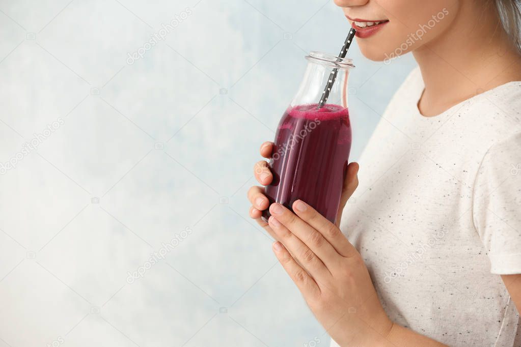 Woman holding bottle of beet smoothie on light background with space for text, closeup
