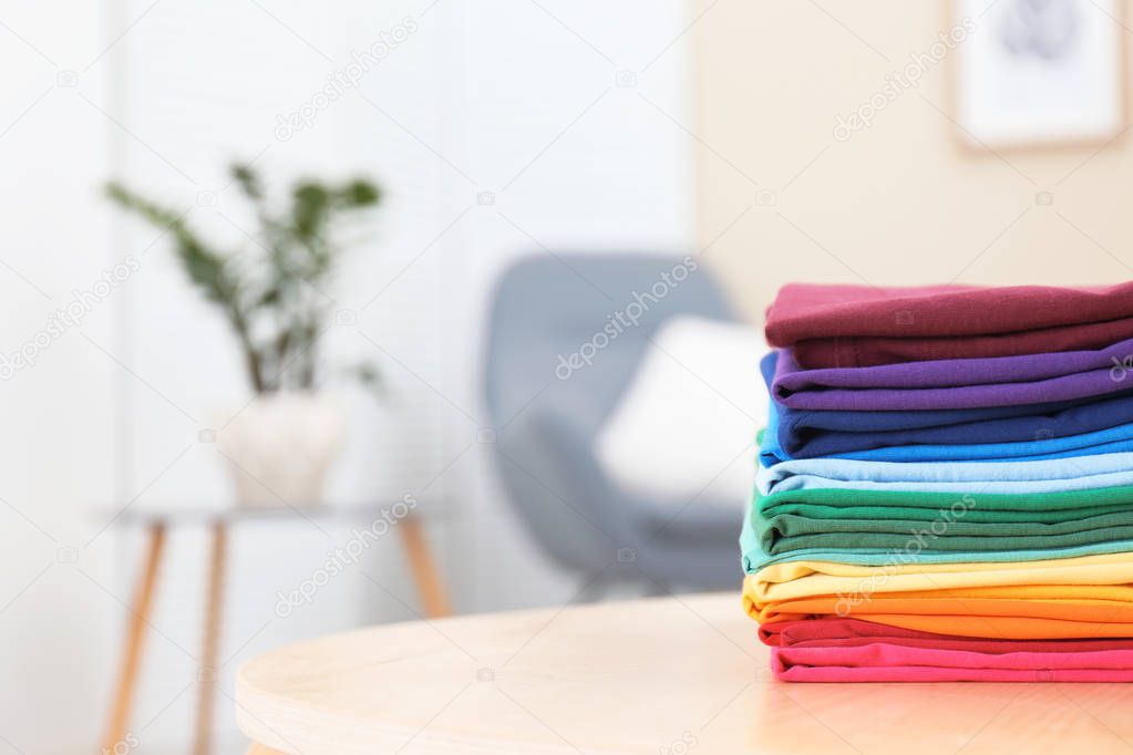 Woman folding bright clothes on table indoors. Rainbow colors