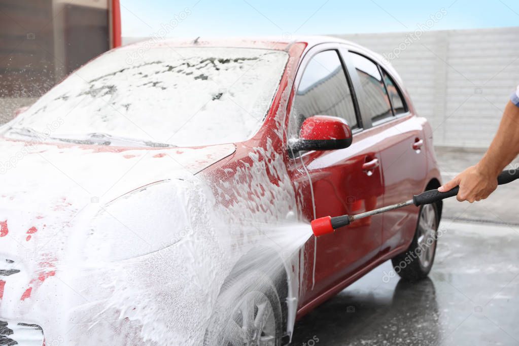 Man foaming red auto at car wash. Cleaning service