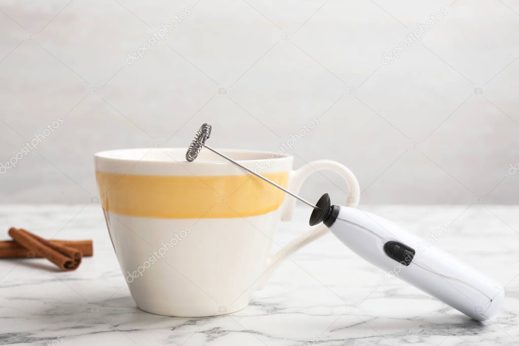 Modern milk frother device and cup on table
