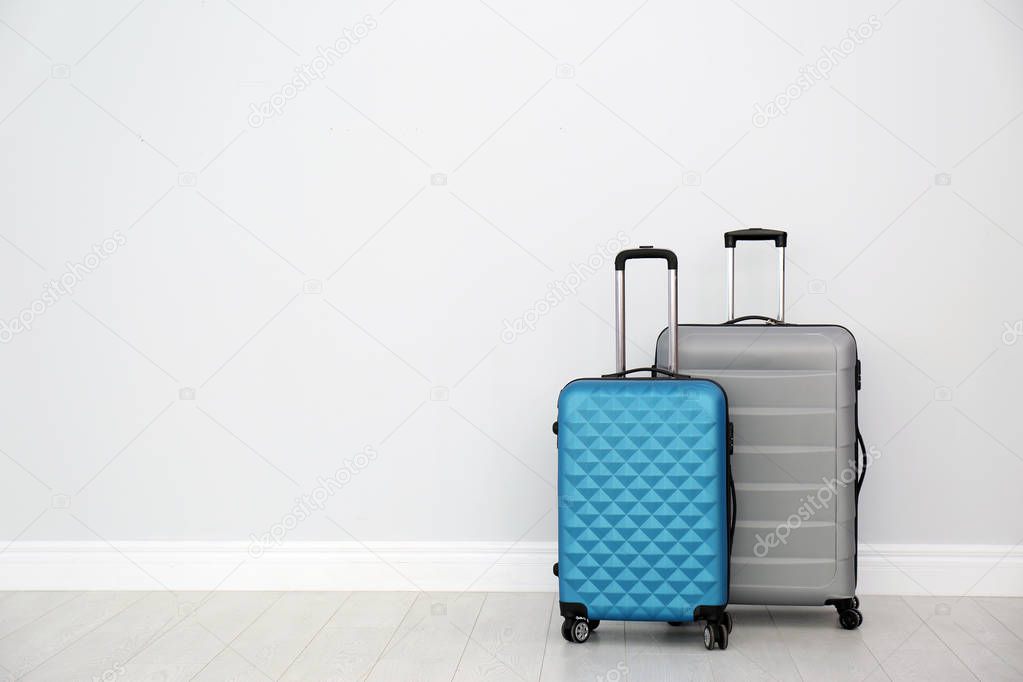 Modern suitcases on floor near light wall. Space for text