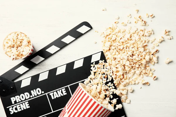 stock image Tasty popcorn and clapperboard on wooden background, top view. Cinema snack