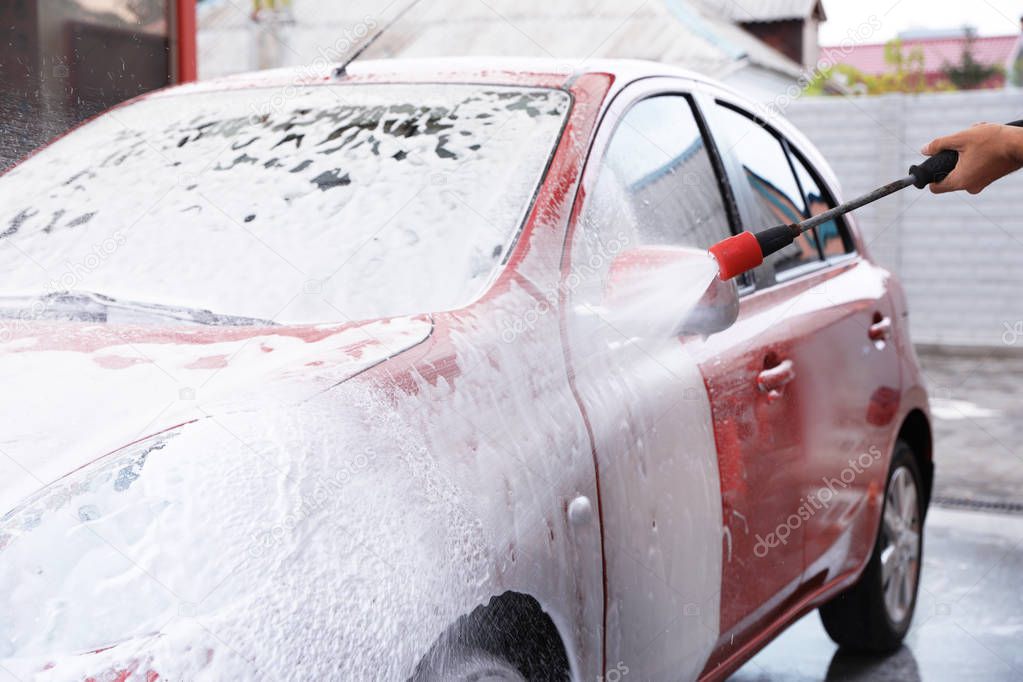 Man foaming red auto at car wash. Cleaning service