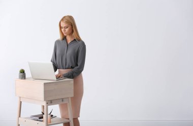 İşyeri beyaz duvar karşı ayağa, dizüstü bilgisayar kullanan genç kadın. Metin için yer
