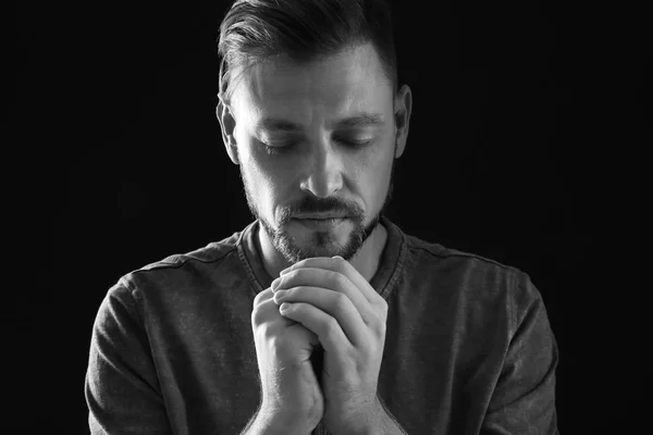 Man with hands clasped together for prayer on dark background, black and white effect