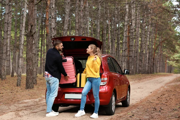 若いカップルが林道に車のトランクにスーツケースを読み込む — ストック写真