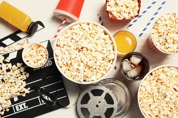 Flat lay composition with popcorn, cinema clapperboard and film reel on light background