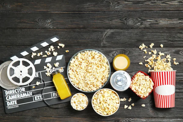 Flat lay composition with popcorn, cinema clapperboard and space for text on wooden background