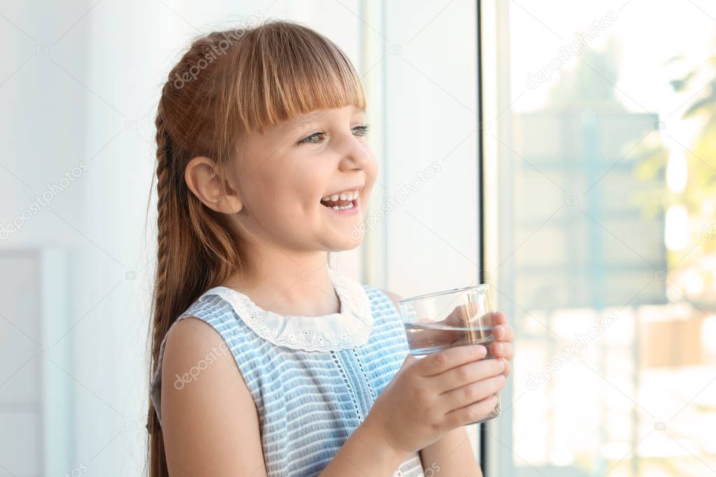 Cute little girl holding glass of fresh water at home