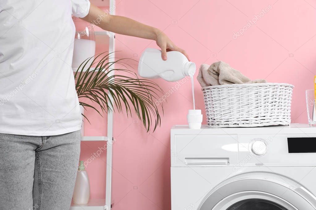 Woman pouring liquid detergent into cap on washing machine in laundry room, closeup