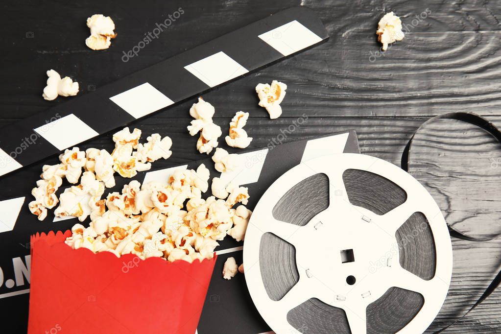 Tasty popcorn, film reel and clapperboard on wooden background, top view. Cinema snack