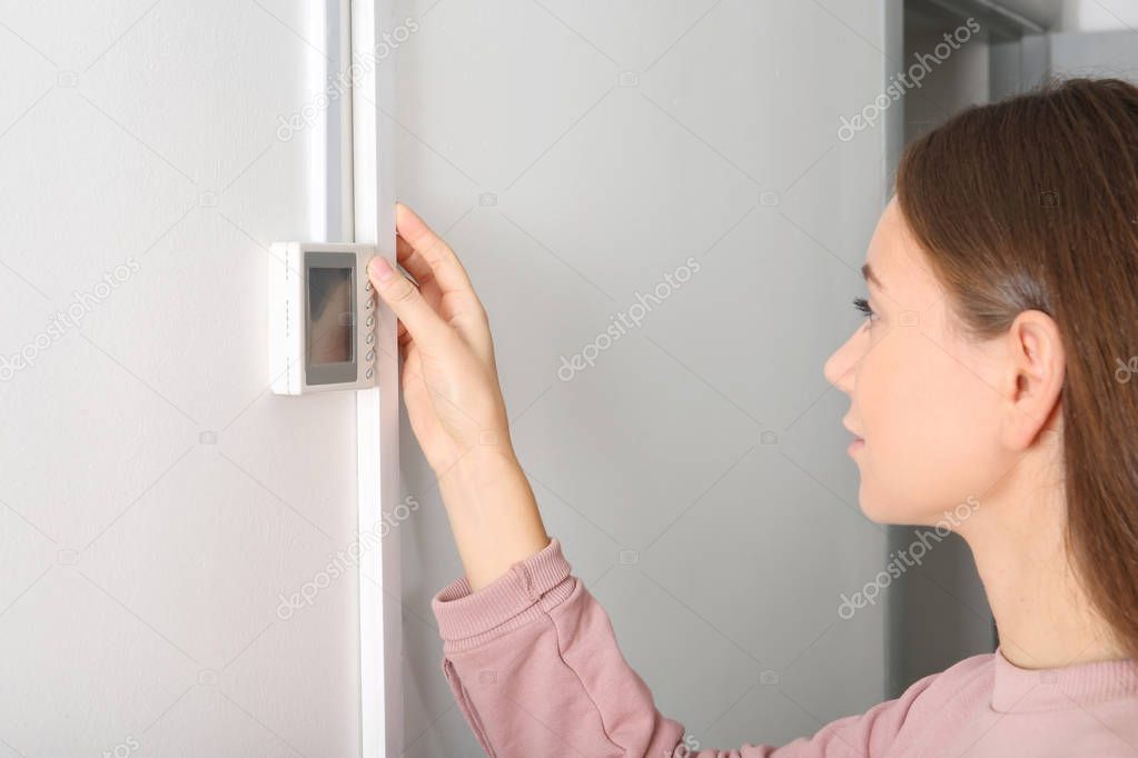 Woman adjusting thermostat on white wall. Heating system