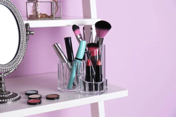 Organizer with cosmetic products for makeup on shelf near color wall