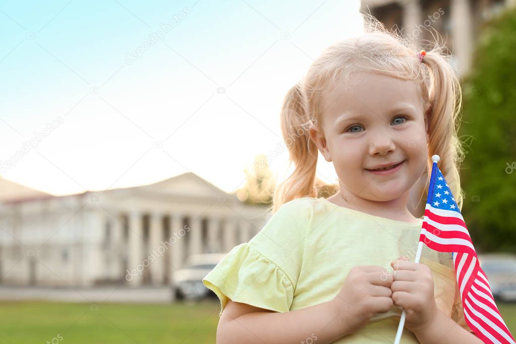 Cute little girl with American flag on city street. Space for text