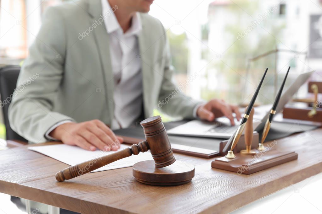 Wooden gavel and blurred notary with laptop on background