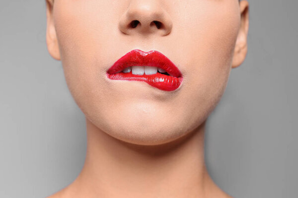 Beautiful young woman with red glossy lips on gray background, closeup