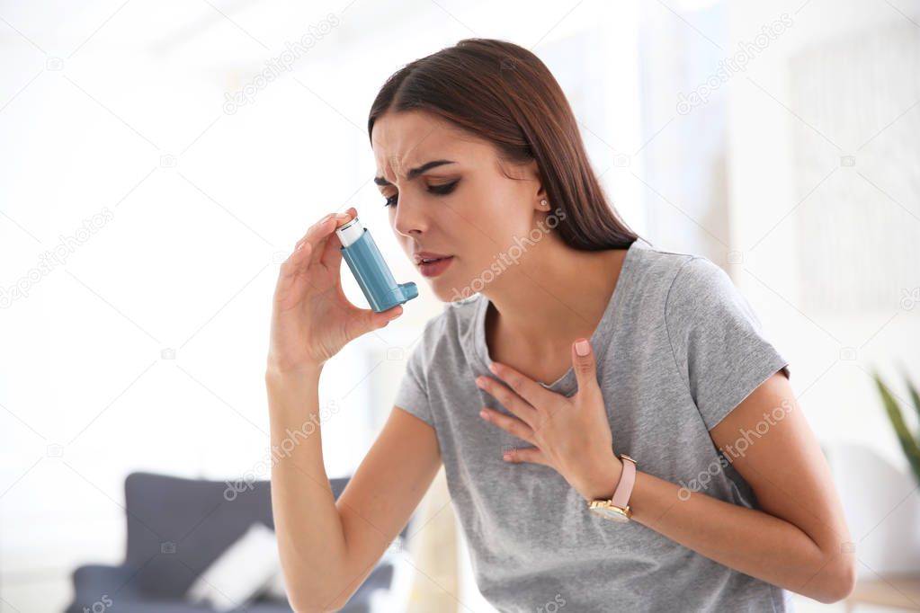 Young woman with asthma inhaler in light room