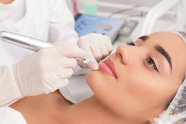 Genç kadın dövme salonu, closeup kalıcı dudak makyaj prosedürü geçiren